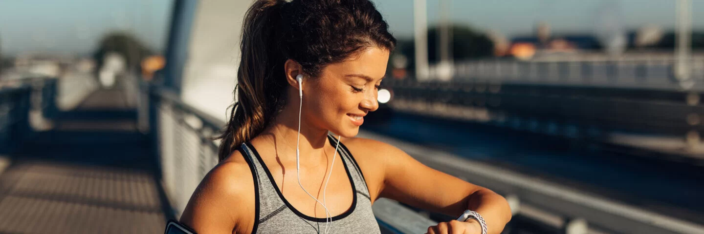 Eine junge Frau schaut beim Joggen auf ihre Smartwatch.