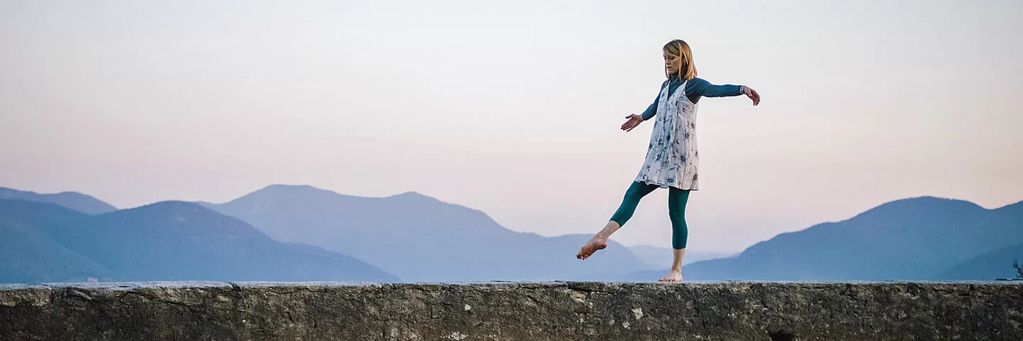 Eine Frau trainiert im Freien auf einer Mauer ihr Gleischgewicht.