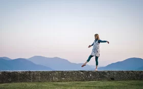 Eine Frau trainiert im Freien auf einer Mauer ihr Gleischgewicht.