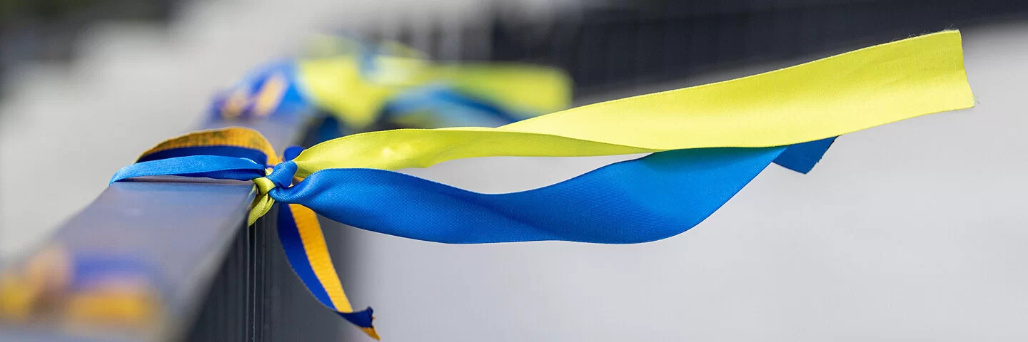 Bänder in den Farben der Nationalflagge der Ukraine sind an ein Geländer einer Brücke gebunden.