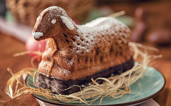 Auf einem Holztisch steht ein Teller mit einem frischen Osterkuchen in Lammform.