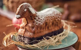 Auf einem Holztisch steht ein Teller mit einem frischen Osterkuchen in Lammform.