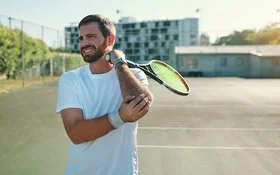 Ein Mann auf dem Tennisplatz fasst sich mit schmerzerfülltem Gesicht an seinen Tennisarm.