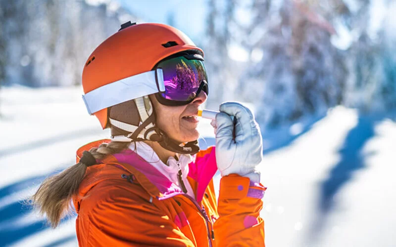 Eine Frau mit Skihelm trägt Lippenbalsam mit UV-Schutz auf die Lippen auf.