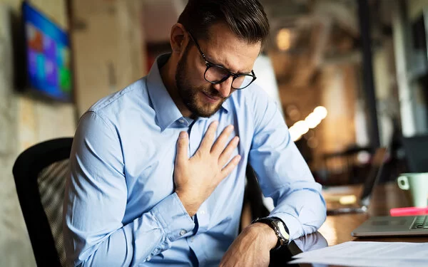 Ein Mann sitzt am Schreibtisch, seine rechte Hand auf die Brust gelegt.