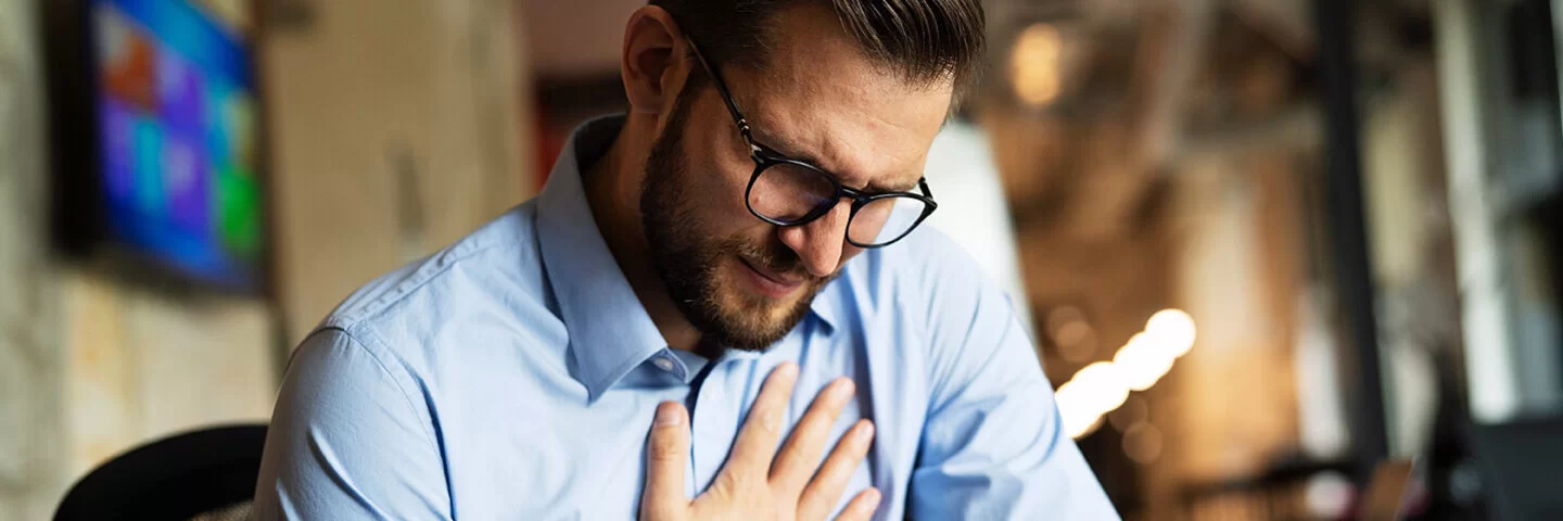 Ein Mann sitzt am Schreibtisch, seine rechte Hand auf die Brust gelegt.