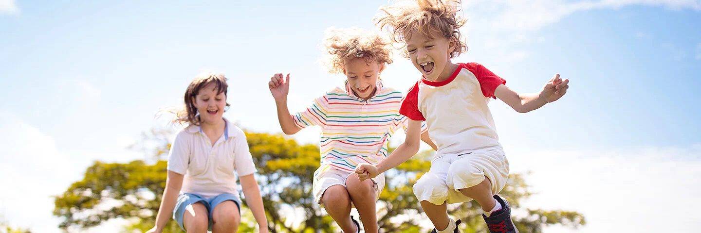 Drei Kinder springen im Sommer auf einer Wiese.