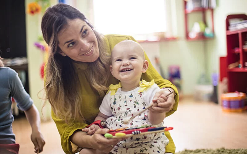 Eine Mutter spielt mit ihrem Baby auf dem Schoß mit einem Spielzeug, das Musik macht.