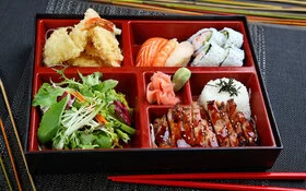 Klassische japanische Bento-Box mit 5 unterschiedlich großen Fächern mit Sushi, Teriyaki-Huhn, Tempura-Shrimps und Salat.
