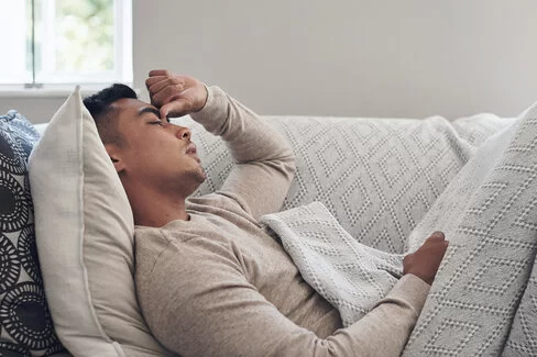 Ein junger Mann liegt auf einer Couch. Er wirkt erschöpft und ruht sich aus.