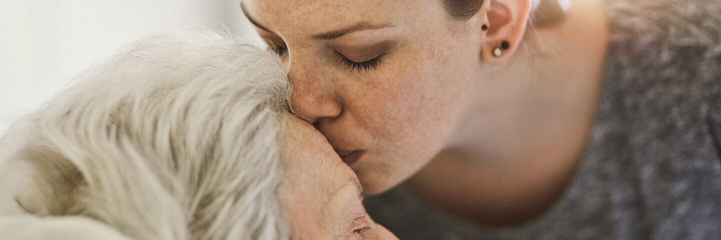 Tochter pflegt ihre kranke sowie bettlägerige Mutter und gibt ihr einen Kuss auf die Stirn.