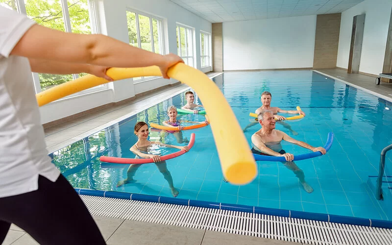 Eine Gruppe trainiert mit Schwimmnudeln im Wasser.