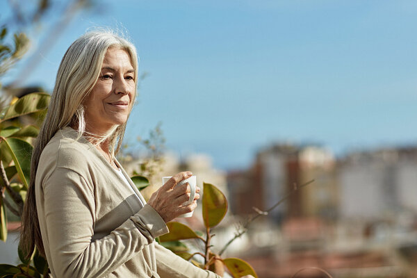 Eine ältere Frau nimmt sich zur Stressbewältigung eine Auszeit, mit einer Tasse Kaffee in der Natur.