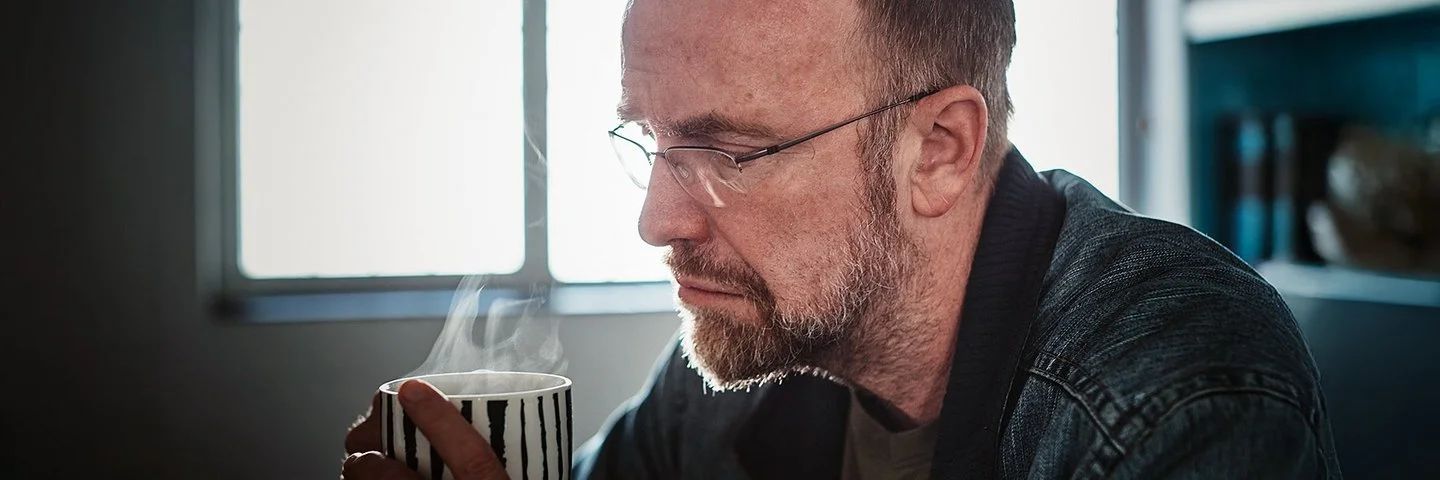 Ein Mann um die 50 mit Midlife-Crisis trinkt resigniert einen Kaffee.