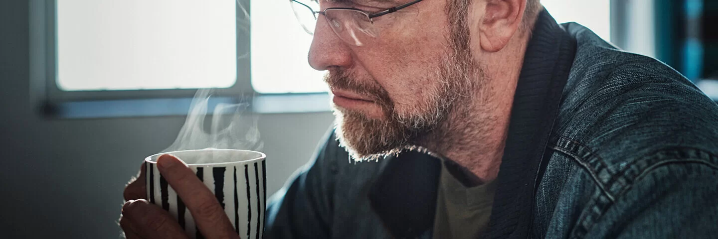 Ein Mann um die 50 mit Midlife-Crisis trinkt resigniert einen Kaffee.