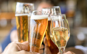 Freunde sitzen im Biergarten und stoßen mit alkoholischen Kaltgetränken an.