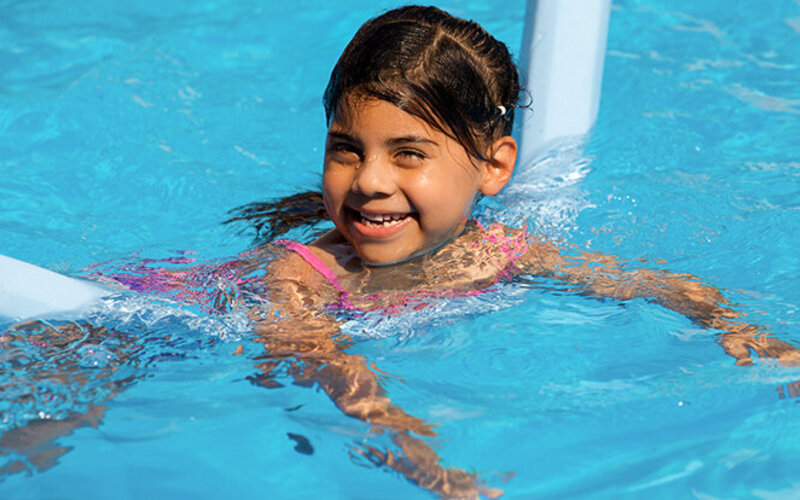 Ein Mädchen schwimmt im Pool mit einer Badenudel.