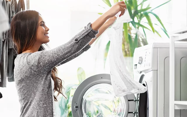 Eine junge Frau nimmt frisch gewaschene und fleckenfreie Wäsche aus der Waschmaschine.