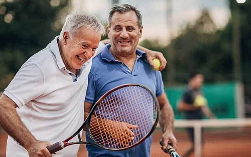 Zwei ältere Männer spielen zusammen Tennis trotz Blasenschwäche.