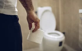 Ein Mann mit einer Rolle Toilettenpapier in der Hand geht auf eine Toilettenschüssel zu.
