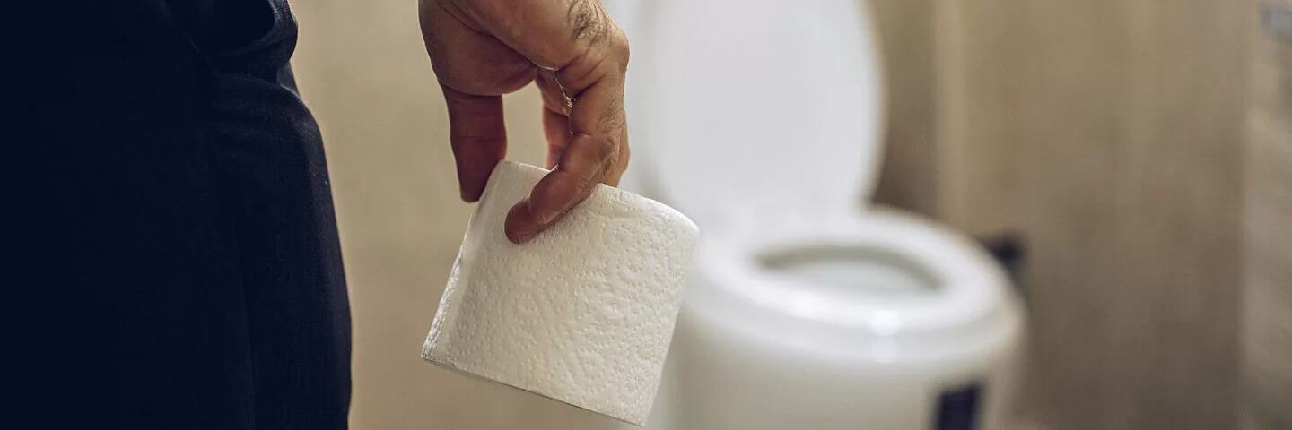Ein Mann mit einer Rolle Toilettenpapier in der Hand geht auf eine Toilettenschüssel zu.