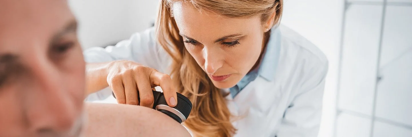 Eine Hautärztin untersucht die Haut eines Patienten mit einem Dermatoskop.