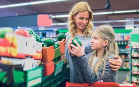 Eine Mutter sucht mit ihrer Tochter in einem Lebensmittelladen Avocados aus.