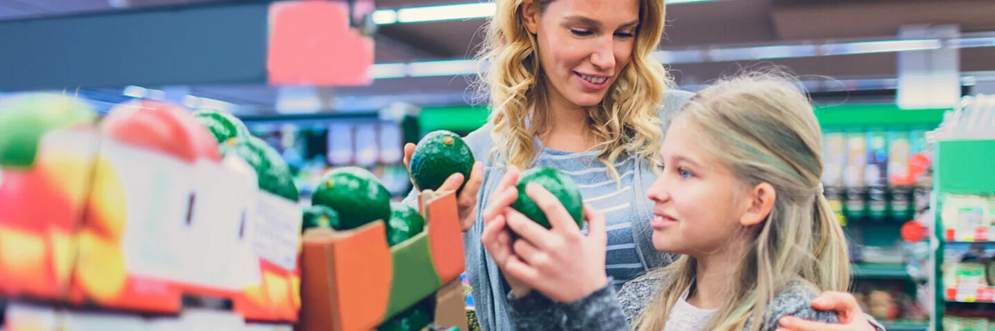 Eine Mutter sucht mit ihrer Tochter in einem Lebensmittelladen Avocados aus.