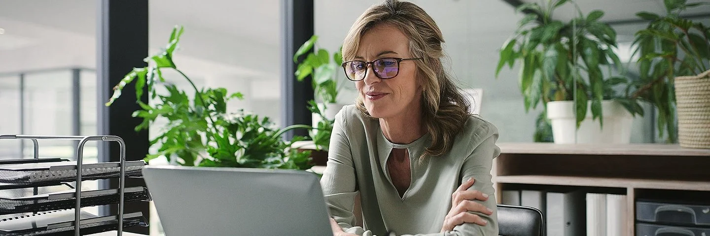 Ein Frau sitzt an einem Schreibtisch und arbeitet an einem Laptop.