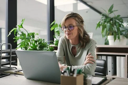 Ein Frau sitzt an einem Schreibtisch und arbeitet an einem Laptop.