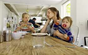 Mutter mit Kindern am Esstisch zu Hause.