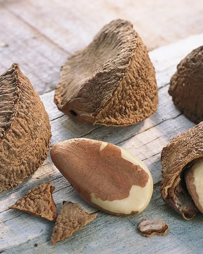 Auf einem Holztisch liegen Paranüsse. Einige haben noch ihre Schale, andere sind bereits geknackt.