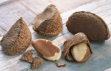 Auf einem Holztisch liegen Paranüsse. Einige haben noch ihre Schale, andere sind bereits geknackt.