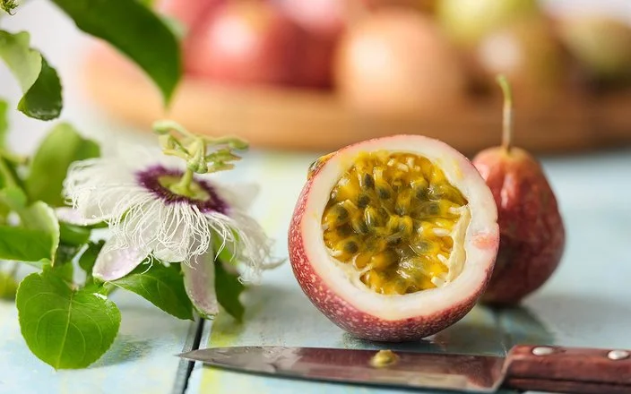 Eine Passionsfrucht liegt durchgeschnitten auf einem Tisch. Das Fruchtfleisch und die Kerne sind gut zu erkennen.