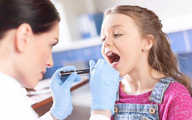 Ein Mädchen mit einer Rachenentzündung wird von einer HNO-Ärztin untersucht.