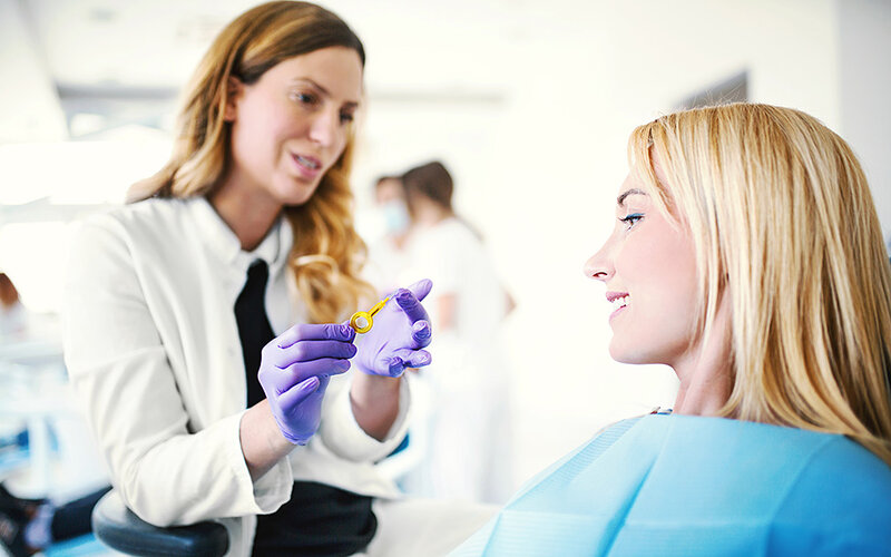 Einer jungen Frau im Untersuchungsstuhl wird der richtige Umgang mit Interdentalbürsten zur Zahnzwischenraumreinigung durch eine Prophylaxefachfrau gezeigt.