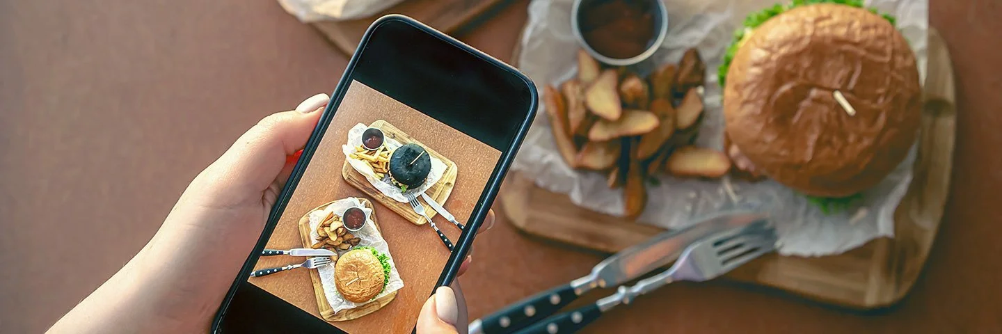 Eine Frau fotografiert mit dem Smartphone ein Burgergericht.