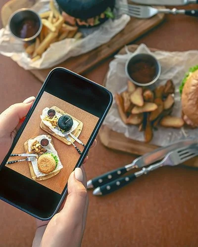 Eine Frau fotografiert mit dem Smartphone ein Burgergericht.