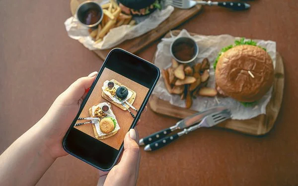 Eine Frau fotografiert mit dem Smartphone ein Burgergericht.