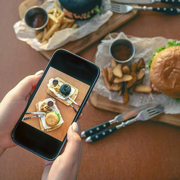 Eine Frau fotografiert mit dem Smartphone ein Burgergericht.