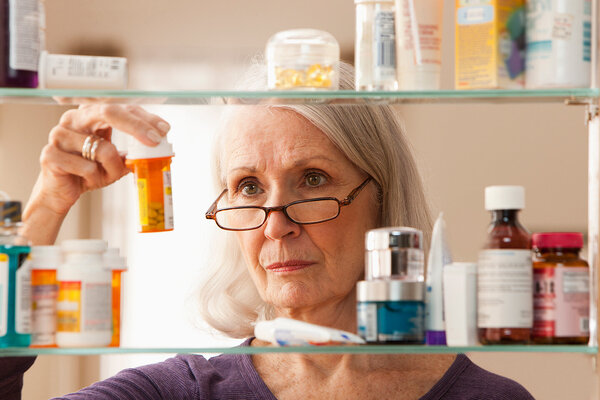 Senioren mit Lesebrille hält ein Medikament ihres Medizinschrankes in der Hand.