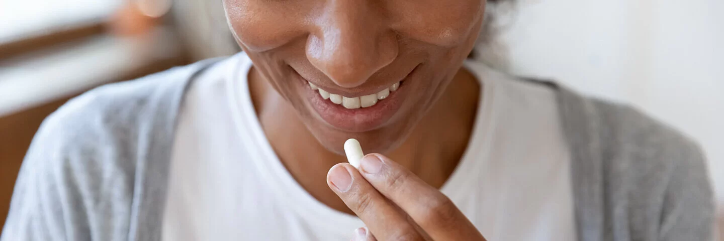 Eine junge Frau hält ein Glas Wasser und eine Tablette (orale Probiotika) in der Hand.