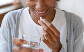 Eine junge Frau hält ein Glas Wasser und eine Tablette (orale Probiotika) in der Hand.