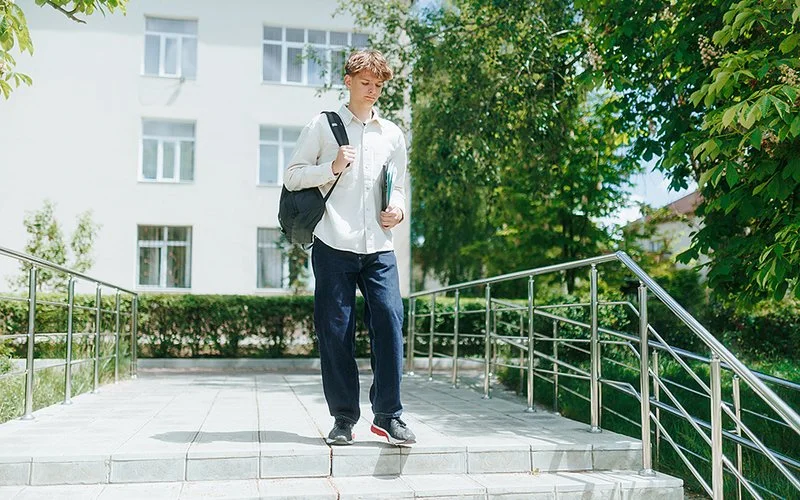 Ein Jugendlicher trägt einen Rucksack und hält Hefter in der Hand. Er geht eine Treppe herunter.