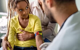Ein Kinderarzt nimmt eine Blutprobe bei einem dunkelhäutigen Mädchen.