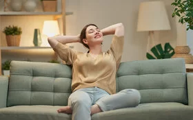 Eine Frau sitzt auf der Couch und fühlt sich glücklich und gesund in ihrem Körper.