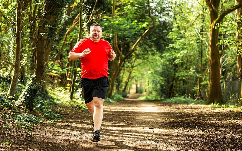 Mann mit Übergewicht joggt auf einem Waldweg.