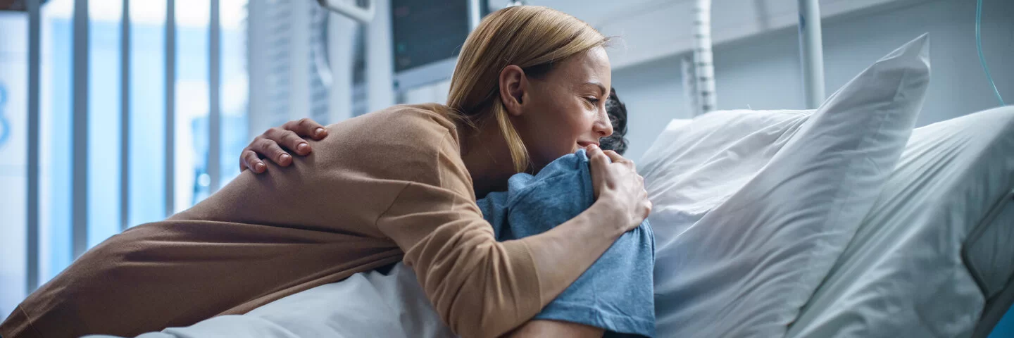 Eine Frau umarmt einen Mann, der in einem Krankenhausbett liegt.