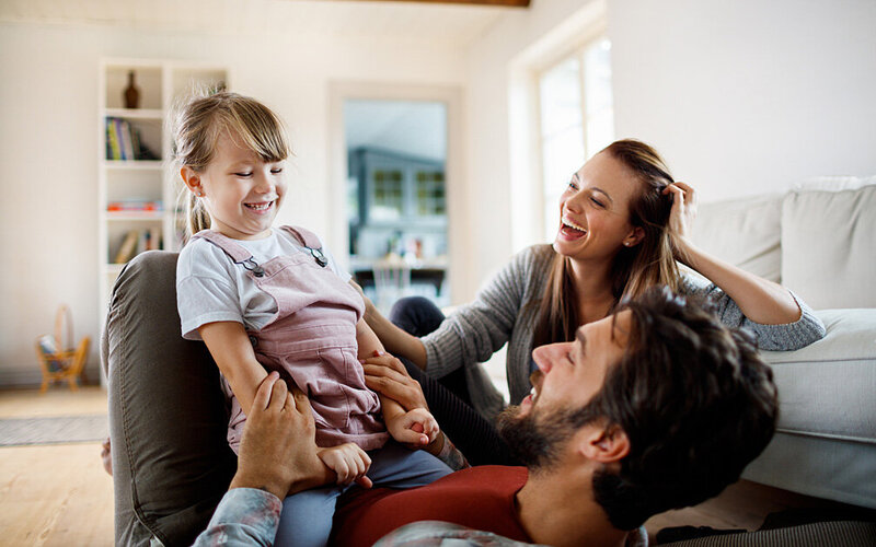 Dreikköpfige Famile hat den Stress im Alltag im Griff und lacht gemeinsam.