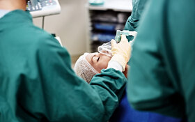 An einem OP-Tisch gibt ein Anästhesist über eine Atemmaske einer Patientin Sauerstoff.